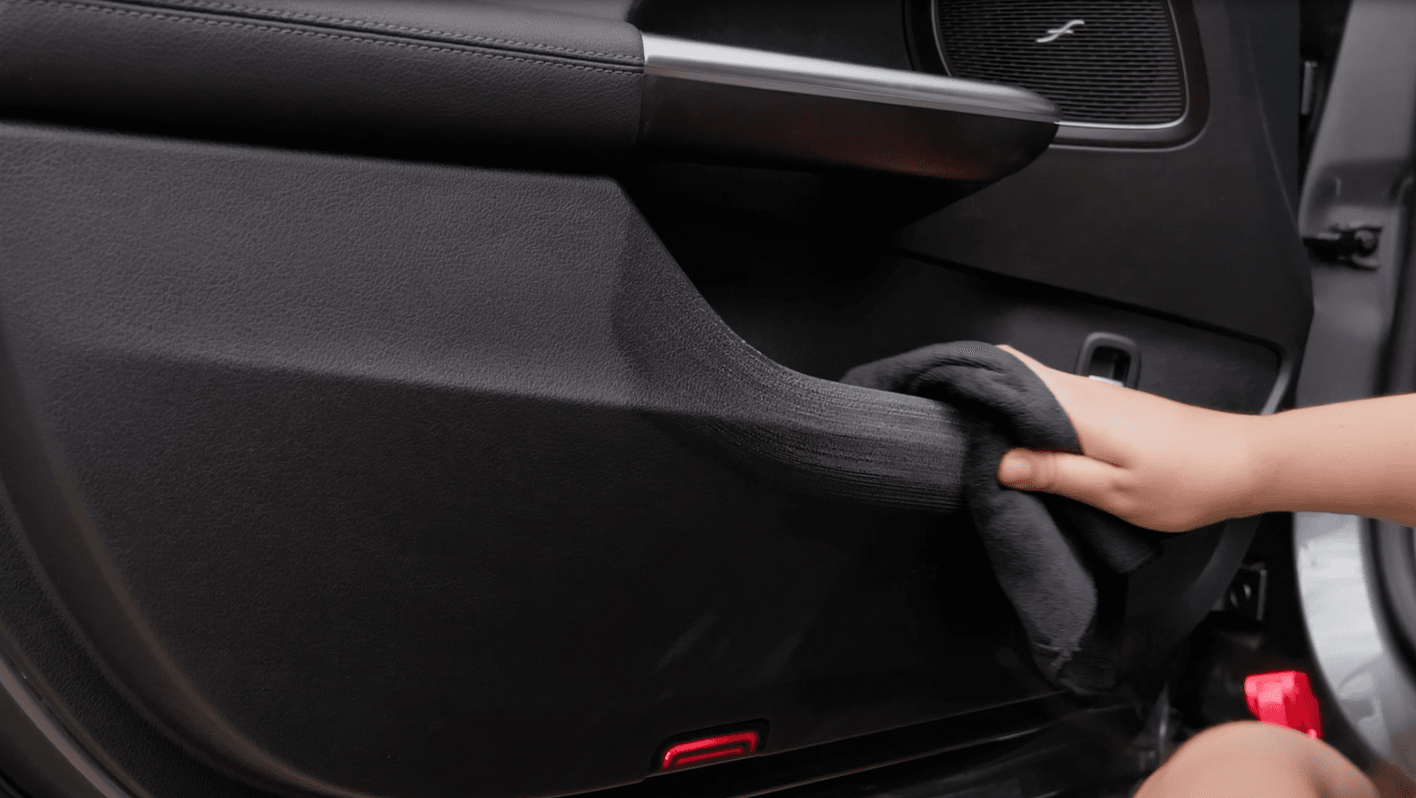 Plastic part of a car door being cleaned with a black microfiber towel.