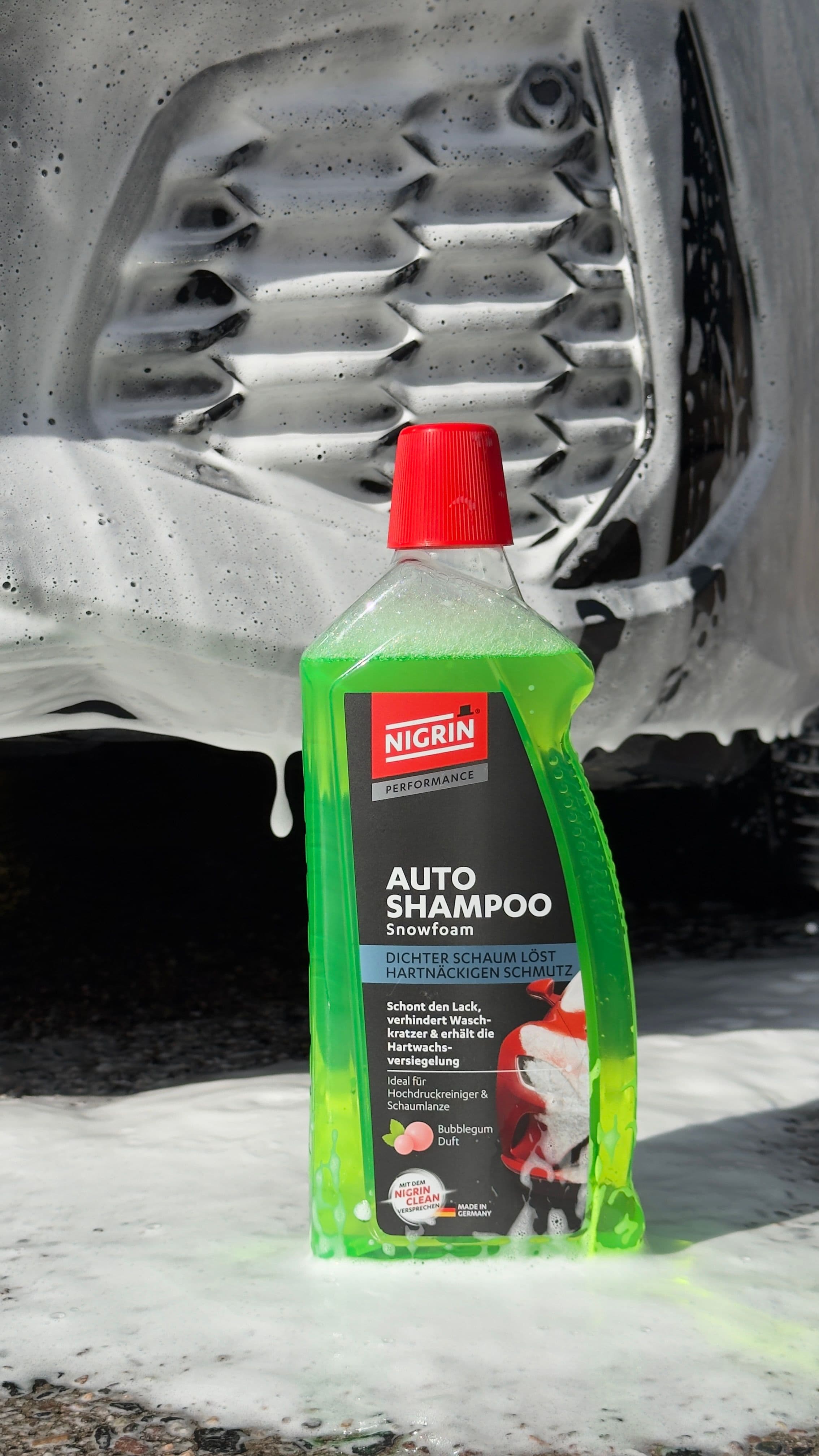 Nigrin Autoshampoo vor einem mit weißen Snowfoam bedeckten Auto
